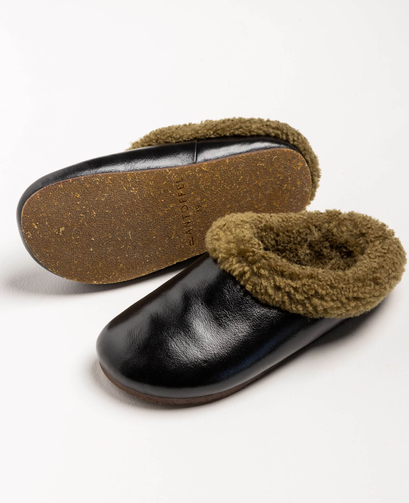 Pantoffel Muti slippers in black leather with a rich brown sheepskin lining, blending sophistication with cozy warmth.